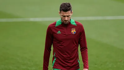 A frustrated, dark-haired FC Basel midfielder, 25, in a plain dark red and green training top, stands waist-up, eyes cast...