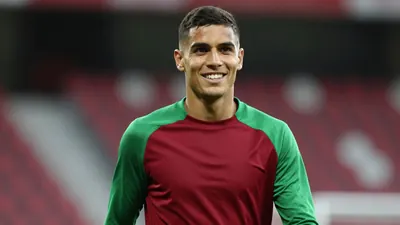 Mid-20s athletic winger, lean build, short dark hair, intense eyes, smiling confidently, waist-up in a plain dark-red and...