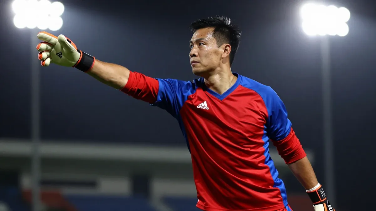 A 25-year-old male goalkeeper with a muscular build, wearing a red and blue jersey, making a save with his outstretched hand