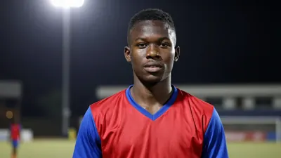 A young, dark-haired, 18-year-old Ghanaian midfielder with a muscular build, wearing a red and blue jersey, photographed...