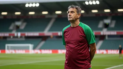 A 35-year-old male head coach with a weathered complexion, wearing a dark red and green plain cotton training top, stands...