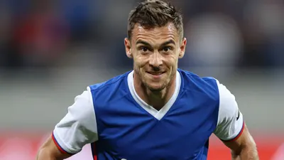 A photorealistic image of a 38-year-old man in a blue FC Basel jersey with white sleeves and a white collar, looking...