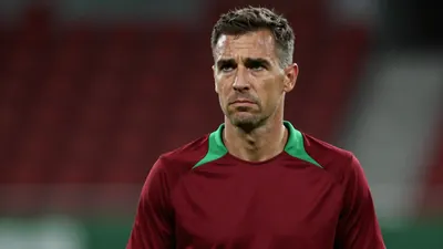 Mid-30s male Basel coach, athletic build, intense eyes, slight frown, wearing a plain dark-red and green training top...