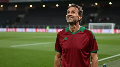A 35-year-old male FC Basel coach, wearing a plain dark red and green polyester training top, stands on the St