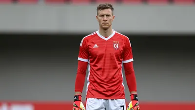 A photorealistic image of an anonymous 37-year-old goalkeeper in a red and white striped jersey with a white collar and...