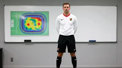 A tight waist-up shot of an anonymous FC Basel coach, wearing a white shirt with a red collar, a black shorts and socks...