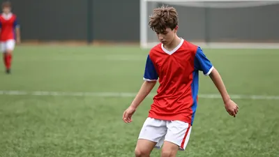 A photorealistic image of an anonymous 16-year-old player with a messy brown haircut, wearing a red and blue jersey made...