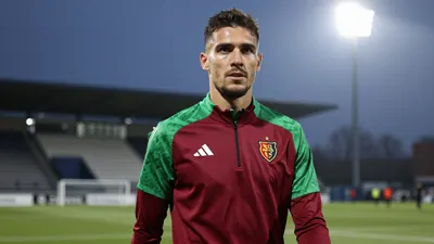 A determined, athletic FC Basel midfielder, aged 25, with a strong build, wears a plain dark red and green training top...