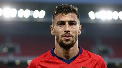 A mid-30s anonymous Basel player in a red training kit, head-and-shoulders portrait, background blurred stadium lights
